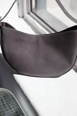 Cartera tipo lady bag color lila, de cuero sintético, con correa ajustable y herrajes metálicos plateados.