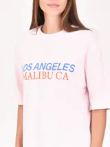 Remera rosa de corte holgado con estampado frontal que dice 'Los Angeles Malibu CA' en azul y naranja.