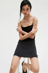 Vestido corto negro de breteles finos, escote cuadrado, corte ajustado y frunces laterales que generan un efecto drapeado en la falda.