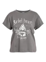 Camiseta gris con estampado frontal de un corazón alado en llamas, con la frase "Rebel Heart" en la parte superior y "Rock You Forever" en la parte inferior.