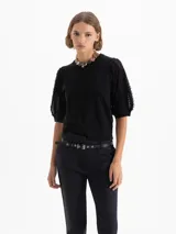 Top negro de largo a la primera cadera con mangas bombachas que incorporan flecos, aportando movimiento y textura al diseño. Confeccionado en una mezcla de hilados que combinan suavidad y estructura.