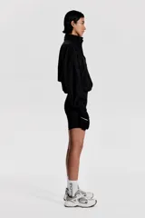 Campera negra de nylon repelente al agua y rompevientos con cuello elevado, cierre con protección para el mentón y bolsillos laterales con cierre. Modelo con hombros caídos, orificios de ventilación en las sisas y mangas murciélago con puños elásticos. Panel de ventilación en malla en la parte baja de la espalda y cordón para ajustar elástico con topes en el bajo. Forro de malla.