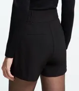Bermuda blanca de poliéster con cintura elástica, cierre con cremallera y botones, y bolsillos laterales.