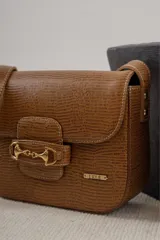 Bandolera color beige con textura símil reptil, cierre con broche metálico dorado y correa larga regulable.