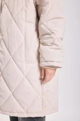 Campera larga color crudo con capucha y cierre frontal, diseño acolchado con patrón de rombos.