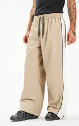 Pantalón deportivo beige de nylon con cintura elástica ajustable con cordón, corte holgado y aberturas laterales con broches.