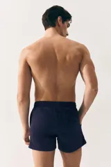 Short de baño azul marino de nylon con elástico revestido y cordón para ajustar oculto en la cintura, bolsillos laterales y bolsillo de solapa con cierre autoadherente atrás. Largo por encima de la rodilla con abertura corta en los laterales y suspensor interior en malla suave.