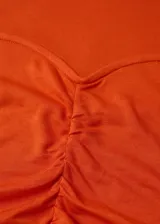 Remera naranja de manga larga con detalle fruncido en el centro y escote redondo.