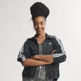 Campera deportiva Adidas Originals modelo Firebird, color negro con estampado animal print sutil. Presenta cuello camisero, cierre frontal y las icónicas tres tiras blancas en las mangas. Lleva el logo del trébol bordado en blanco en el pecho.