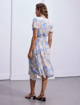 Vestido midi estampado con flores color celeste y beige, escote cruzado, mangas cortas con puños elastizados, cintura elastizada con lazo de ajuste.