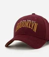 Gorra de sarga color borgoña con bordado frontal de la palabra "Brooklyn" en color dorado.