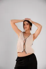 Chaleco tejido color beige con ribete negro en el borde y cierre frontal con botones.