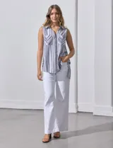 Blusa sin mangas con estampado a rayas verticales en tonos grises y blancos. Tiene cuello camisero, cierre frontal con botones y dos bolsillos con solapa en el pecho.