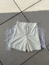 Short blanco de bengalina elastizada con cordones cruzados en la parte delantera y flecos en los laterales.