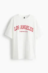 Remera blanca de algodón con estampado rojo de la frase "Los Angeles California U.S.A.", corte oversized, cuello redondo y mangas cortas.