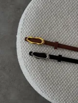 Cinturón fino de ecocuero, con hebilla ovalada irregular metálica.