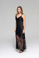 Vestido largo negro de seda con breteles finos y escote en V. Presenta un panel de encaje floral en la parte inferior, con corte asimétrico.