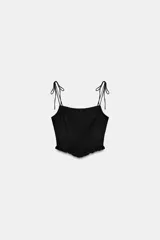 Top crop corsetero negro de popelín con escote recto, tirantes finos ajustables con lazada y bajo acabado con volante. Tiene forro interior a tono y cierre de cremallera en la espalda.