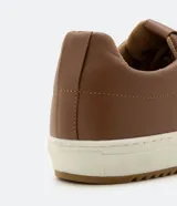 Championes marrones de cuero, con caña baja, ajuste con cordones y suela blanca.