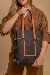 Cartera tipo tote bag color negro, con doble asa de mano y correa bandolera ajustable. Presenta un bolsillo rectangular en el frente.