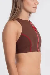 Top de bikini deportivo color marrón chocolate, estilo nadador, con cuello alto y cierre frontal de cremallera roja. Presenta costuras de realce en rojo en los laterales y sisas.