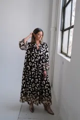 Vestido largo de corte amplio con estampado animal print en tonos negro y beige, cuello camisero y mangas largas.