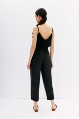 Pantalón sastrero negro de tiro alto confeccionado en cupro y viscosa, con ajuste en el tobillo, bolsillos delanteros y traseros, y pinzas en el frente.