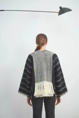 Chaqueta de punto en color negro con detalles en blanco, de frente abierto y diseño holgado. Presenta paneles frontales con patrón de zigzag y terminación de flecos en el ruedo, mientras que las mangas exhiben un motivo de líneas punteadas horizontales.