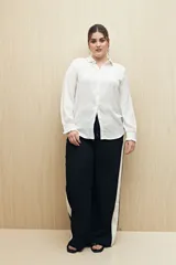 Camisa blanca de manga larga con textura sutil y caída fluida. Presenta cuello clásico, botones forrados a tono y puños con terminación fruncida.