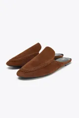 Zapato plano tipo babucha destalonada color marrón, confeccionada en serraje, con detalle de pespuntes en el cerco, copete subido y acabado en punta redonda.