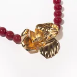 Collar de cuentas color borgoña con dije dorado en forma de flor.