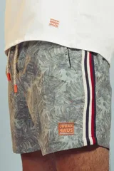 Short de baño con estampado de hojas en tonos grises y celestes, con cordón ajustable en la cintura y detalle de franja lateral con rayas rojas, blancas y negras.