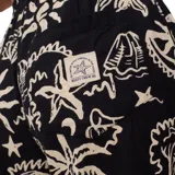 Pantalón de tela negro con estampado de palmeras, soles y estrellas de mar en color beige.