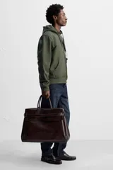 Bolso de mano extragrande color marrón oscuro, fabricado en piel de alta calidad. Tiene un compartimento principal con cierre magnético, un bolsillo interior con cremallera y un bolsillo secundario con solapa y cinta. Las asas son de piel.