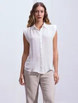 Blusa blanca de gasa marca Tahari, con cuello a la base con solapa, abertura central con botones ocultos y detalle plisado en los hombros.