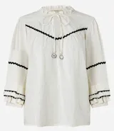 Blusa color crema de tricolina con detalles de ondas negras en cuello, mangas y frente. Tiene mangas 3/4 con volados y lazo en el cuello.