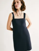 Vestido corto negro con escote cuadrado y tirantes anchos. Tiene bolsillos laterales y corte recto.