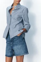 Camisa de cuello solapa y manga tres cuartos con puño ancho. Tiene aberturas laterales en el bajo y cierre frontal con botones ocultos.