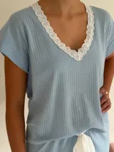 Conjunto de pijama de dos piezas color negro, compuesto por una remera de manga corta con escote en V adornado con puntilla beige, y un short con lazo frontal beige y terminación de puntilla beige en el ruedo.