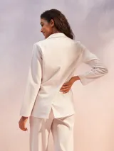 Blazer de mujer color blanco roto o beige muy claro, de corte recto y doble botonadura con botones marrones. Se combina con un top y pantalón a juego del mismo tono.