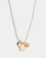 Collar corto con perlas blancas irregulares y dijes colgantes dorados: cristal amatista, rectángulo de nácar, corazón de nácar y dije circular con diseño de corazón y rayos.