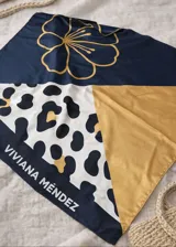 Pañuelo cuadrado de poliéster con diseño estampado a bloques: azul marino con flor dorada, estampado de leopardo en blanco y negro con detalles dorados, y un bloque liso color dorado. Incluye la inscripción "VIVIANA MÉNDEZ" en el borde azul marino.