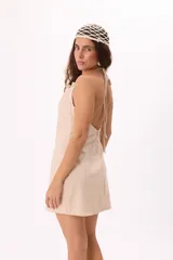 Vestido corto color beige, de escote halter con espalda descubierta y amarre regulable al cuello.