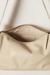 Bolso bandolera color crema, de cuero, con correa ancha ajustable con hebilla dorada.
