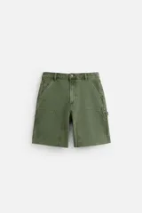 Bermuda color verde militar, de corte relaxed fit, con bolsillos frontales y traseros tipo plaqué, detalle de tira y bolsillo multifunción en la pierna, y bajo irregular.