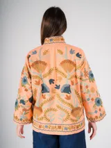 Chaqueta color salmón con bordado floral estilo Suzani en tonos azules, marrones y verdes.
