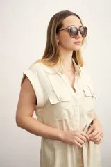Vestido camisero corto color beige, con cuello clásico, mangas cortas con puños, dos bolsillos con solapa en el pecho, cinturón de lazo y cierre frontal con botones.
