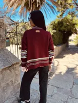 Sweater tejido color borgoña con diseño de copo de nieve en el frente y bordes con motivos geométricos en tonos beige, blanco y marrón.