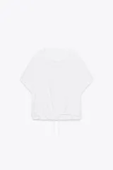 Camiseta blanca de algodón con cuello redondo, mangas cortas y bajo asimétrico ajustable con lazadas.
