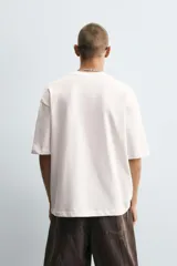 Camiseta blanca de corte holgado, con cuello redondo y mangas cortas. Estampado en el frente con dibujos de gatos, texto en japonés y frases en inglés.